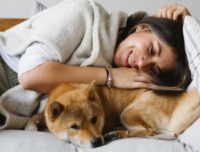 Woman cuddling with her dog in bed, wrapped in a cozy blanket