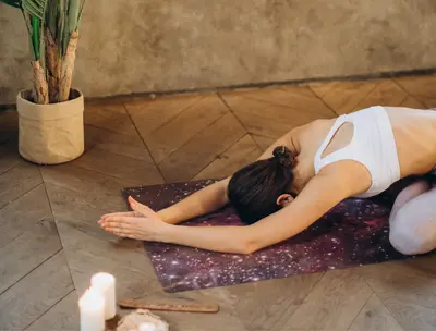 Woman stretching forward on a starry yoga mat surrounded by candles and a potted plant