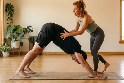 Ava giving a light hands-on cue to a student in Downward-Facing Dog with bent knees