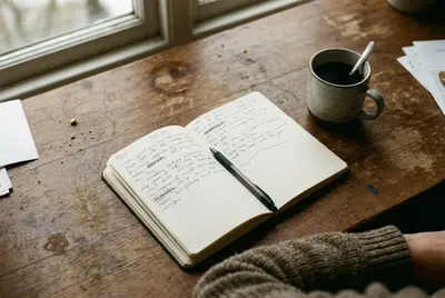 Open notebook with handwritten notes, a pen, and a mug of tea on a wooden table
