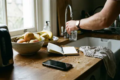 Filling a glass of water at the kitchen sink beside a notebook and a bowl of fruit