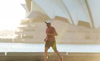 Man jogging along a waterfront path with the Sydney Opera House in the background