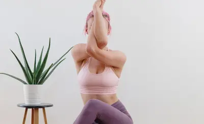 Woman practicing an eagle-arm yoga pose beside a potted aloe plant