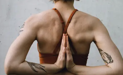 Back view of a woman with tattooed arms holding her hands in reverse prayer position