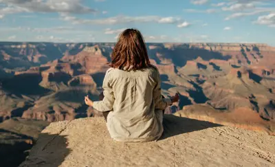 Woman meditating cross-legged at the edge of a canyon overlook