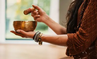 Hand striking a brass singing bowl with a wooden mallet