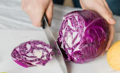 Hands slicing a purple cabbage on a cutting board
